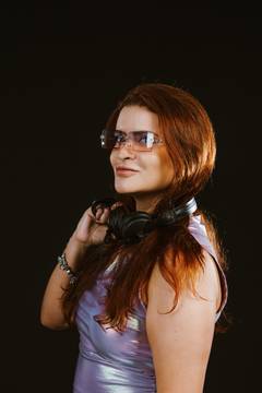 Ga.bih de perfil em top lilás iridescente, fones no pescoço